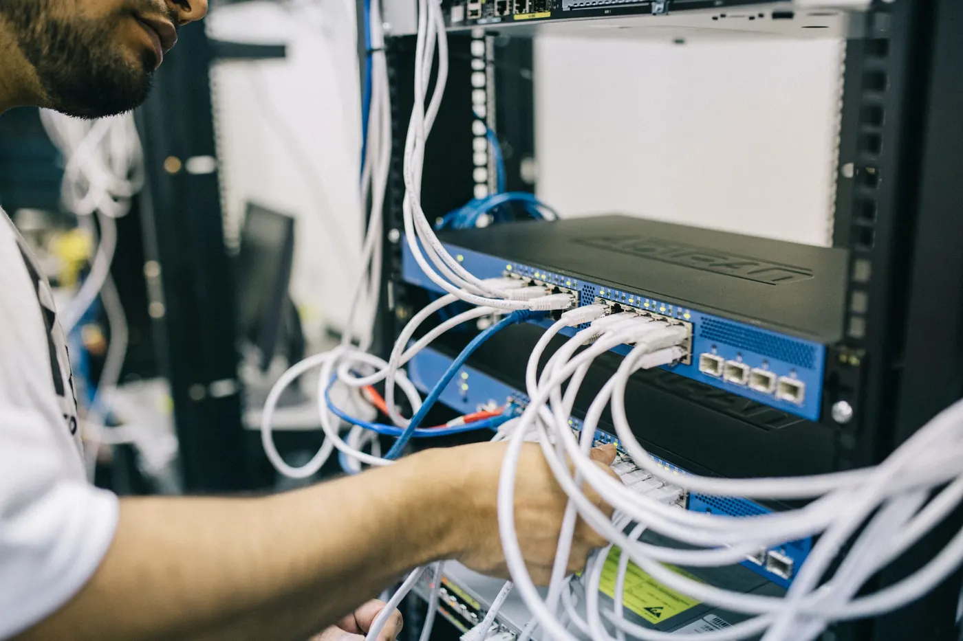 IT technician connecting Ethernet cables to a switch in a network rack